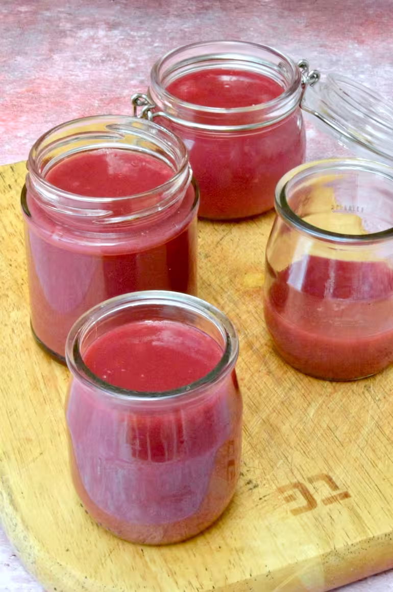 Raspberry rose curd poured into jars on board.