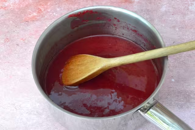 Sugar and lemon stirred into raspberries with wooden spoon.