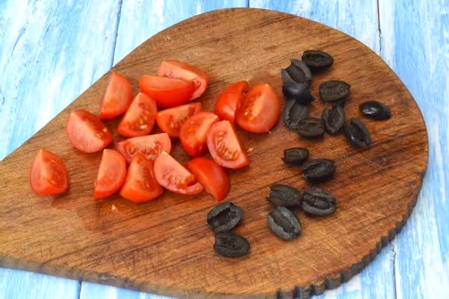 Tomatoes quartered and black olives halved on board.