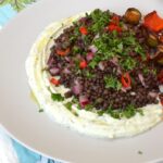 Plate of black lentil salad on bed of whipped ricotta cheese.