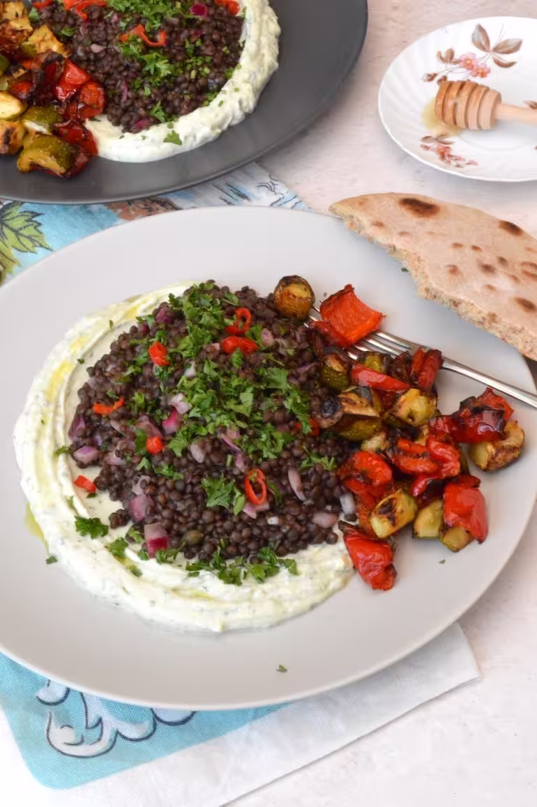 Plate of black lentil salad on herby lemon whipped ricotta with roasted veg and bread on side.