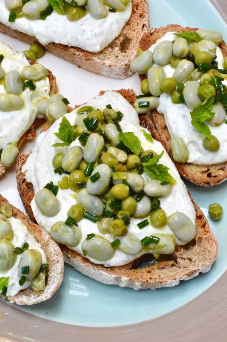 Whipped cottage cheese and broad bean toast slices on platter.