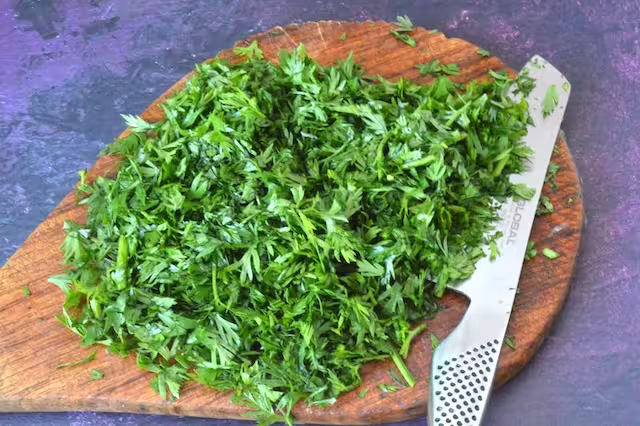 Carrot top fronds chopped on board with knife.