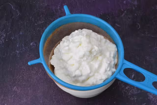Cottage cheese draining through a sieve.