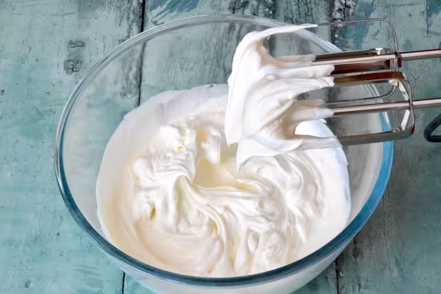 Bowl of whipped double cream with electric beaters.