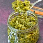 Forkful of homemade fermented kohlrabi with carrot tops taken from open jar.