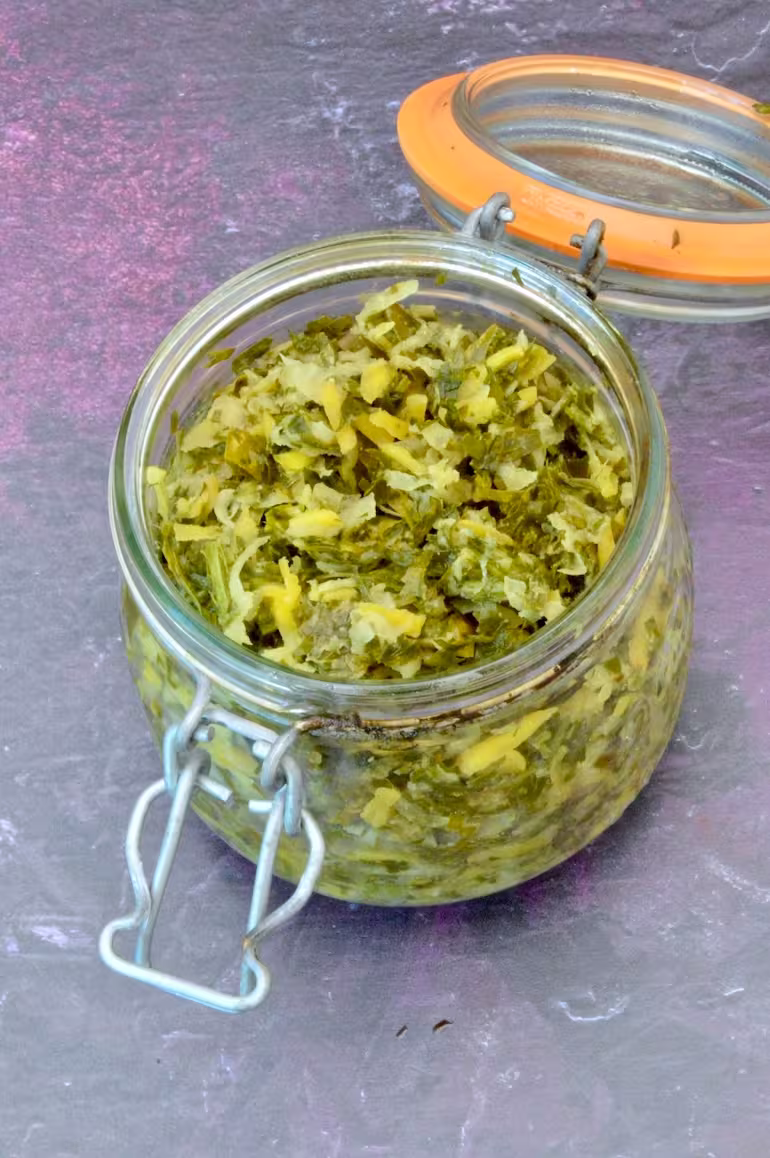 Open clip top jar of homemade fermented kohlrabi and carrot tops.