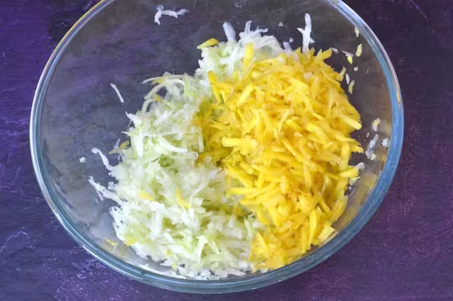 Grated kohlrabi and yellow carrot in mixing bowl.