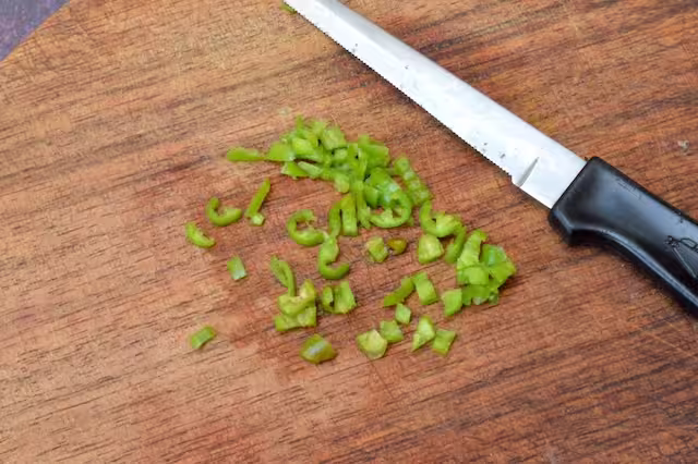 Deseeded green chilli finely chopped on board with knife.