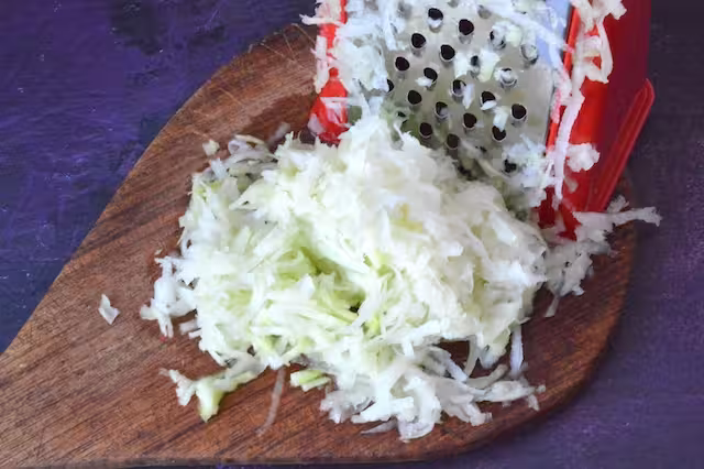 Grated kohlrabi with box grater on board.