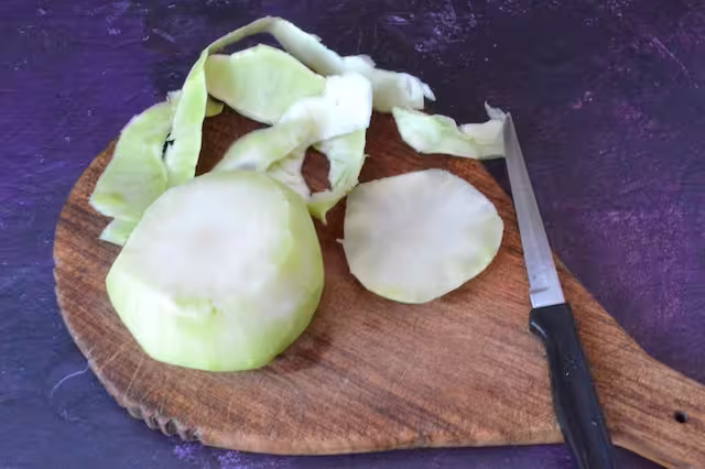 Kohlrabi bulb peeled on board with knife.