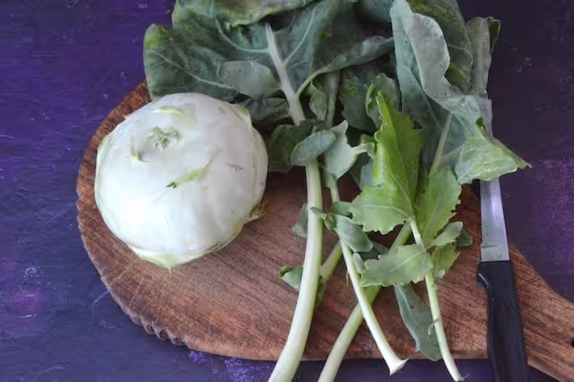 Kohlrabi bulb and leaves on board with knife.