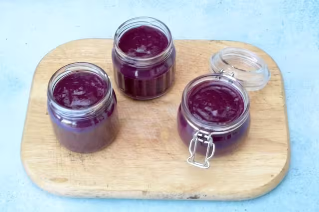 Three open jars of homemade blackberry curd.