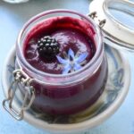 Open jar of homemade blackberry curd with blackberry and borage flower on top.