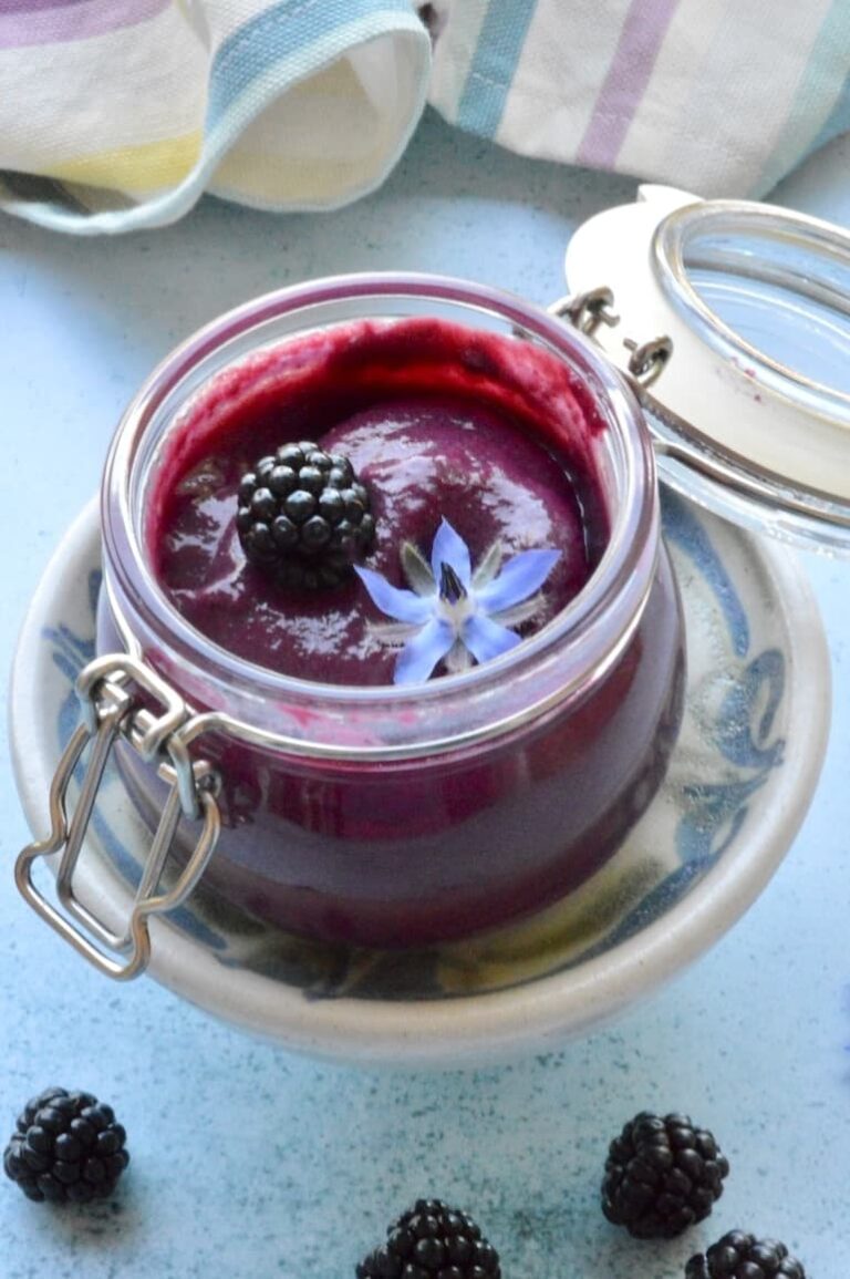 Open jar of homemade blackberry curd with blackberry and borage flower on top.