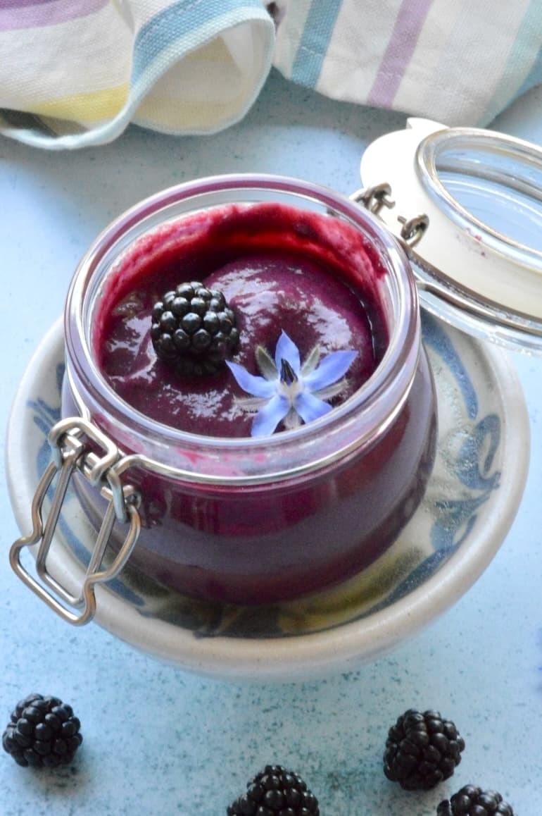 Open jar of homemade blackberry curd with blackberry and borage flower on top.