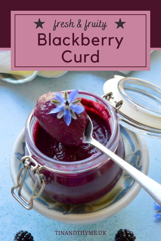 Open jar of homemade blackberry curd with spoonful resting on top with borage flower.
