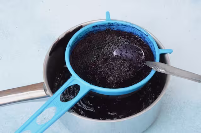 Blackberry seeds in sieve with spoon.