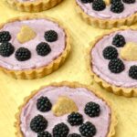 Homemade blackberry tarts with hazelnut pastry cases on wooden board.