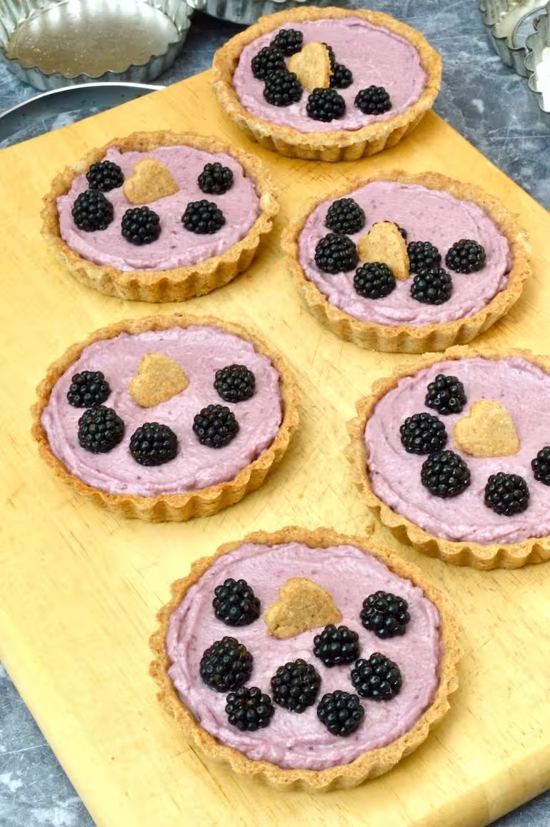 Homemade blackberry tarts on board with empty tart cases behind.