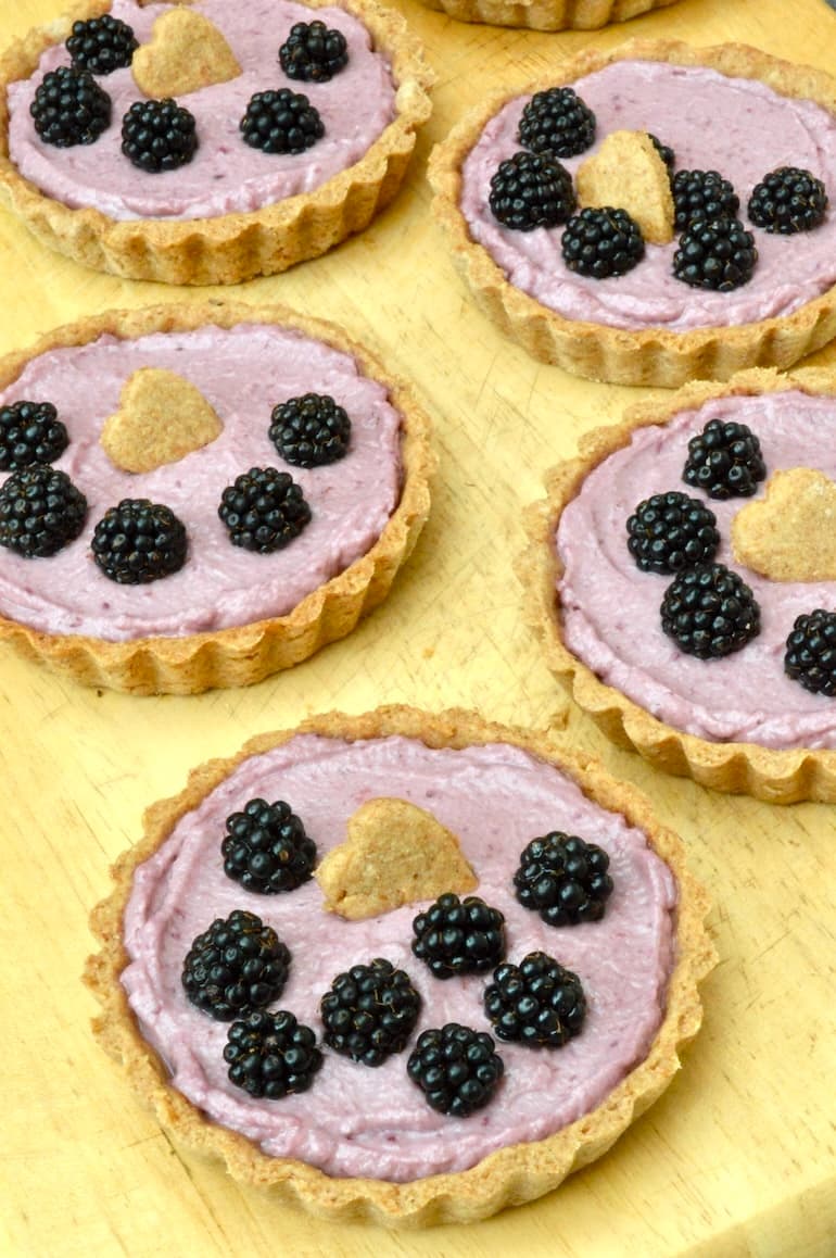 Homemade blackberry tarts with hazelnut pastry cases on wooden board.