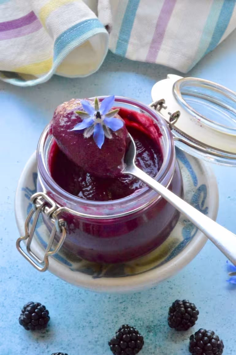 Homemade blackberry curd in clip-tip jar with spoonful resting on top and borage flower.