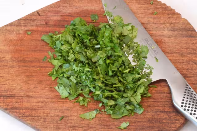 Roughly chopped pile of coriander leaves (cilantro) with knife.