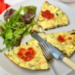 3 slices of courgette and ricotta frittata with tomato sauce on plate with salad, knife and fork.