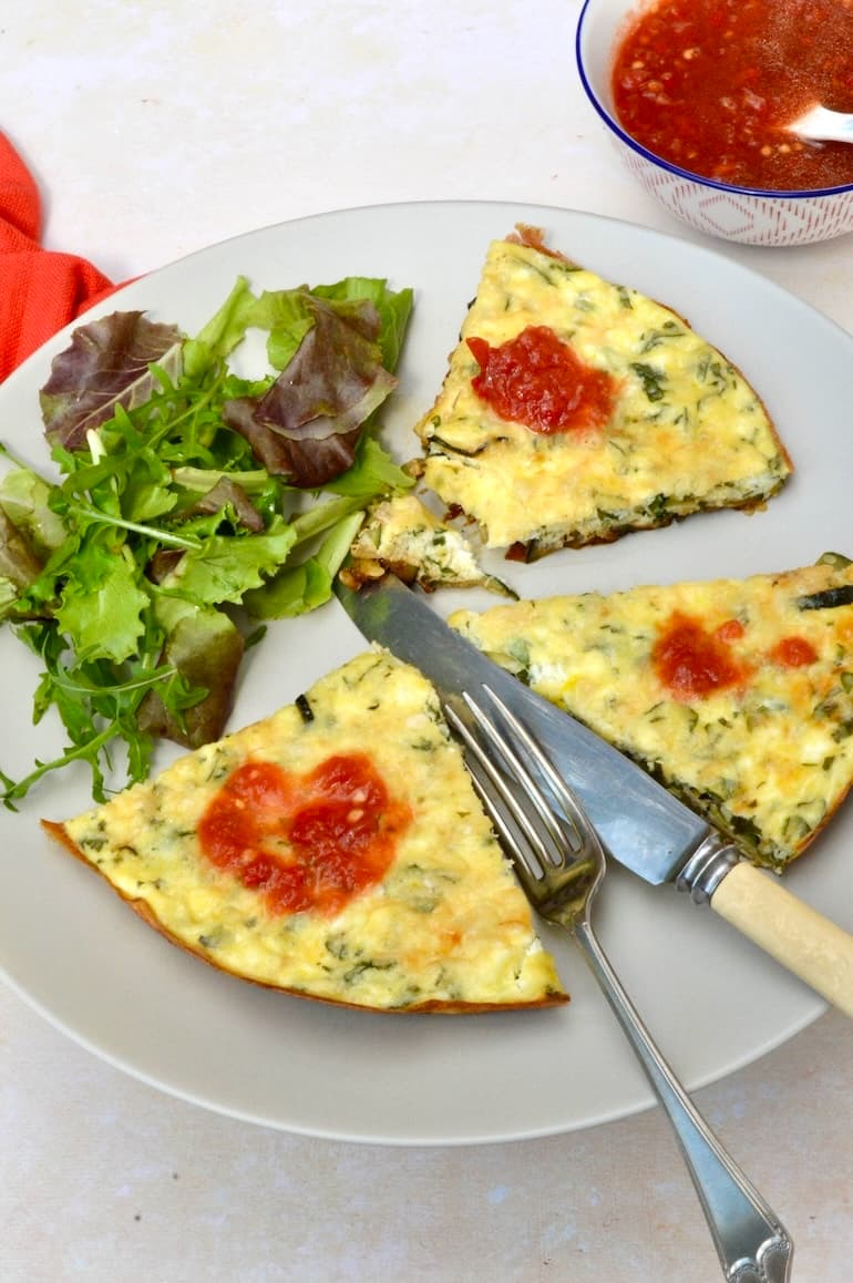 3 slices of courgette and ricotta frittata with tomato sauce on plate with salad, knife and fork.