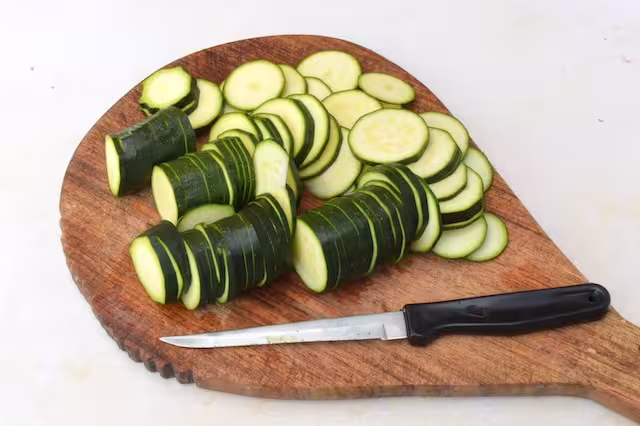 Sliced courgettes on chopping board with knife.