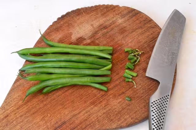 Small bunch of French beans topped on chopping board with knife.