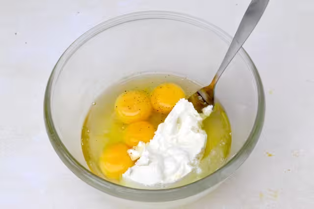 Eggs and ricotta cheese in mixing bowl with fork.