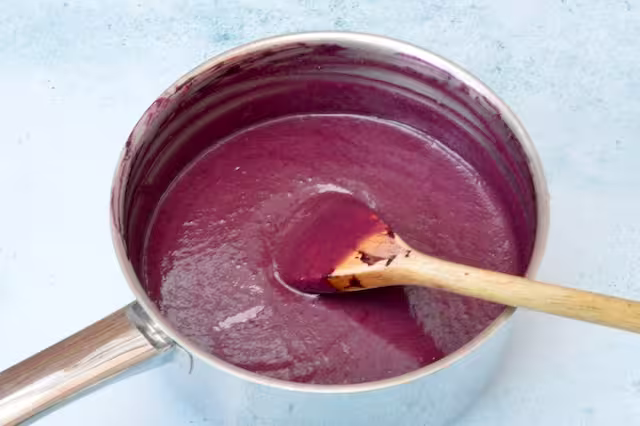 Pan of finished blackberry curd with wooden spoon.