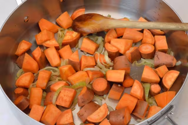 Sweet potatoes and onions frying in pan with wooden spoon.