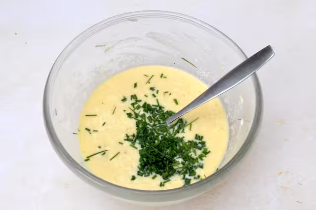 Chives snipped into egg mixture in mixing bowl with fork.