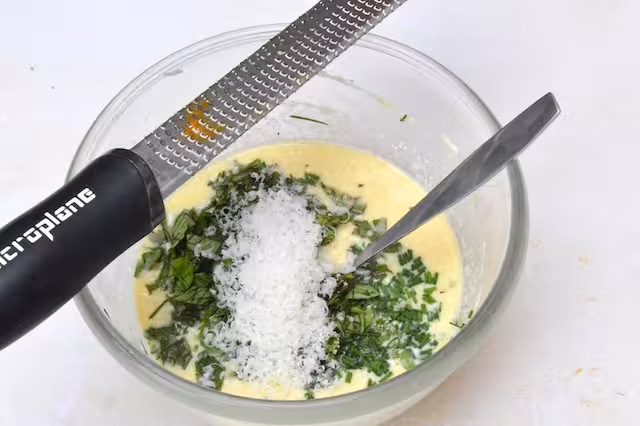 Grated cheese added to mixing bowl with microplane on top.