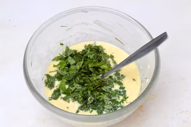 Chopped mint and basil added to beaten eggs in bowl.