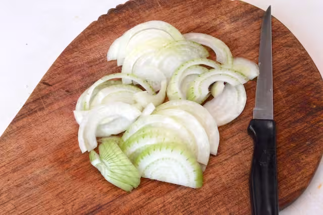 Onion sliced into half moons on chopping board with knife.