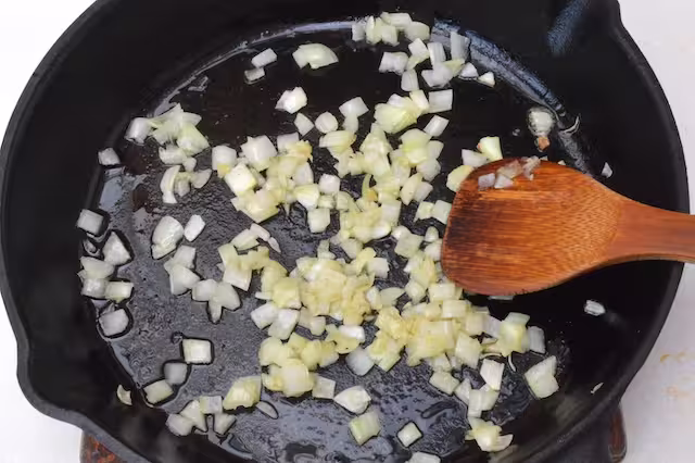 Chopped onions frying in cast iron skillet with wooden spatula.