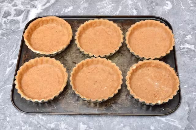 Raw pastry cases in tin on baking tray.