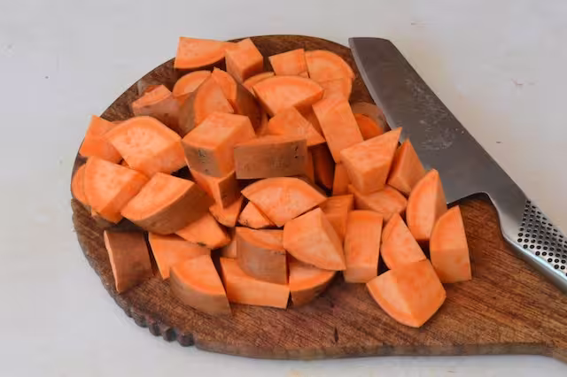Sweet potato chunks on chopping board with knife.