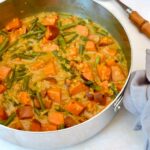 Serving spoon and pan of homemade sweet potato and green bean curry with lentils.