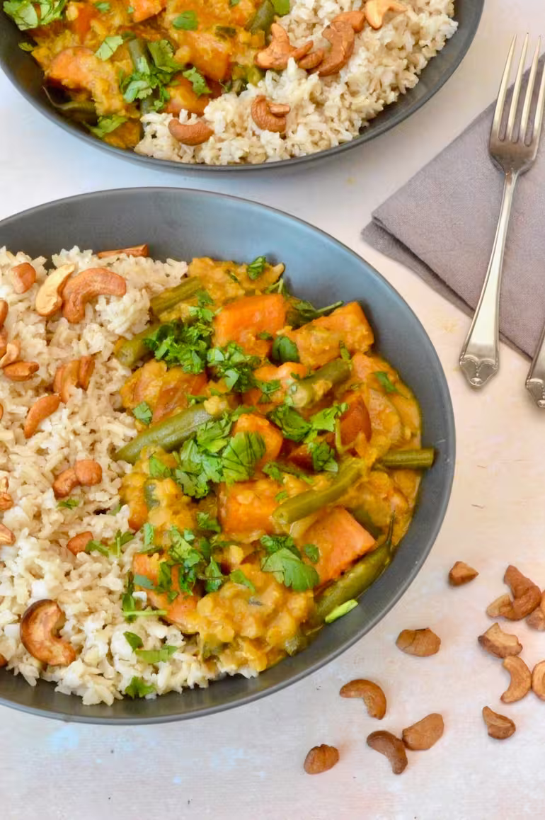 Close up of bowl of green bean and sweet potato curry with rice and cashew nuts.