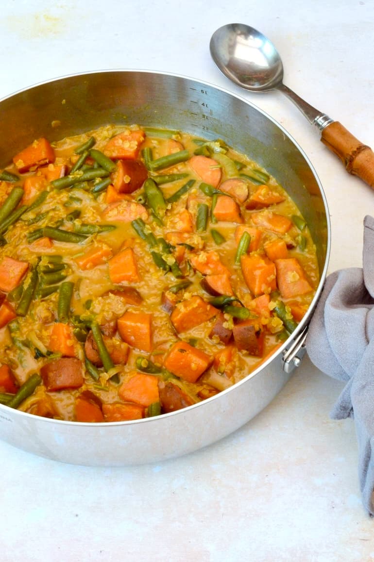 Serving spoon and pan of homemade sweet potato and green bean curry with lentils.