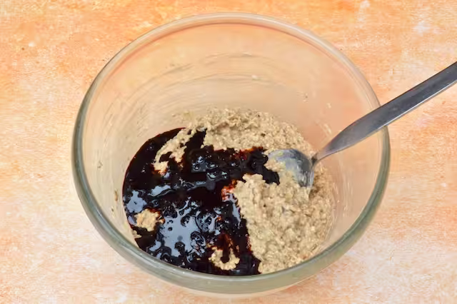 Date molasses added to soaked oats in mixing bowl with spoon.