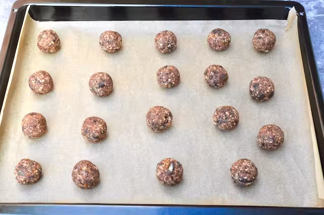 Date and almond dough balls on lined baking tray.