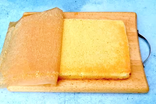 Baking paper partially peeled off genoise on board.