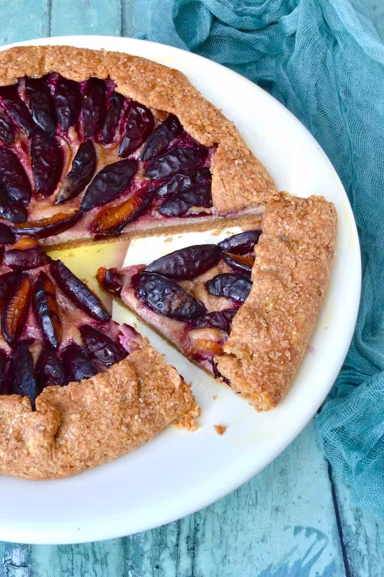 Wholemeal spelt plum galette with ricotta on plate with a slice partially removed.