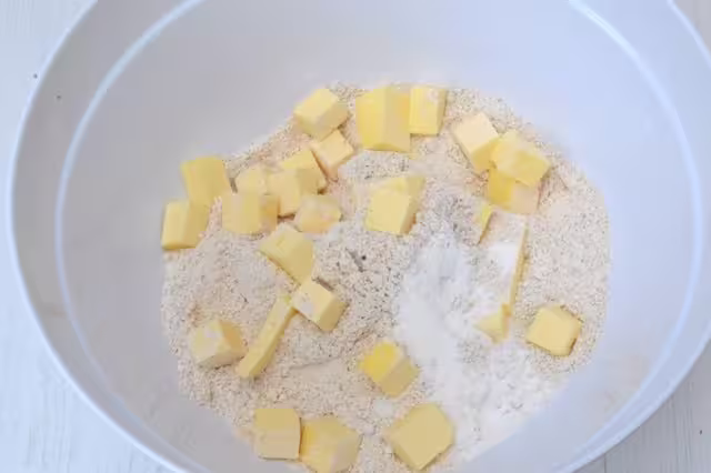 Butter cubes in bowl of flour and baking powder.