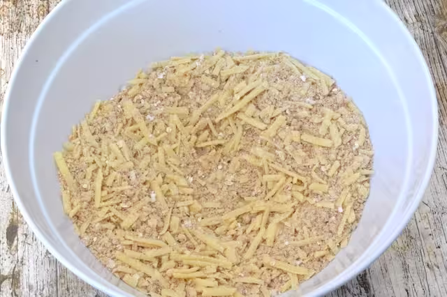 Grated cheese added to raw crumble in bowl.